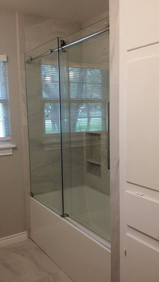 Sliding glass shower door over a white tub with chrome hardware, next to white storage.