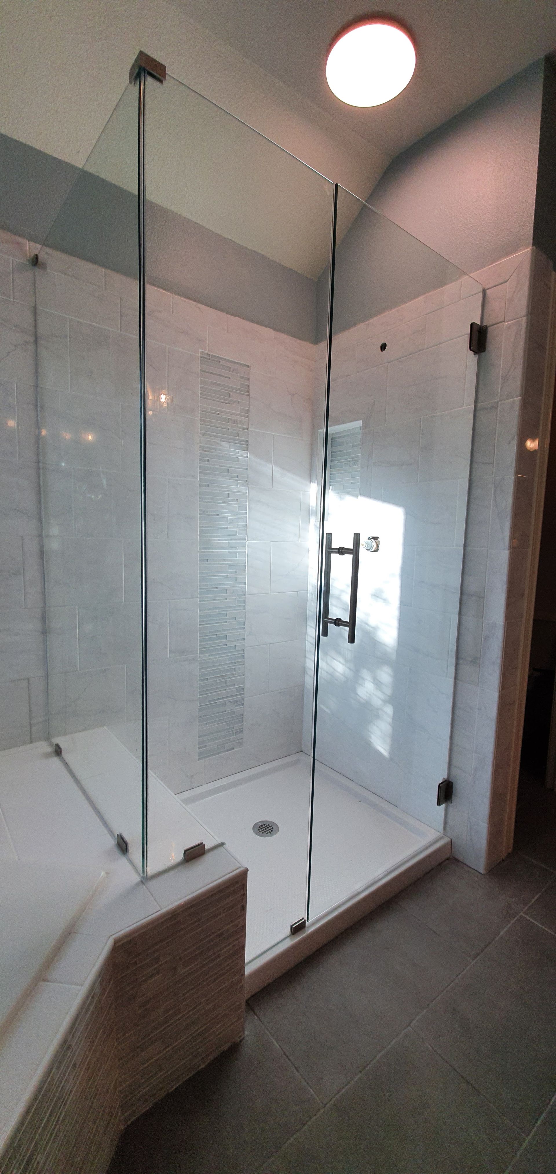 A modern shower with clear glass walls, white tile, and a light-colored floor.