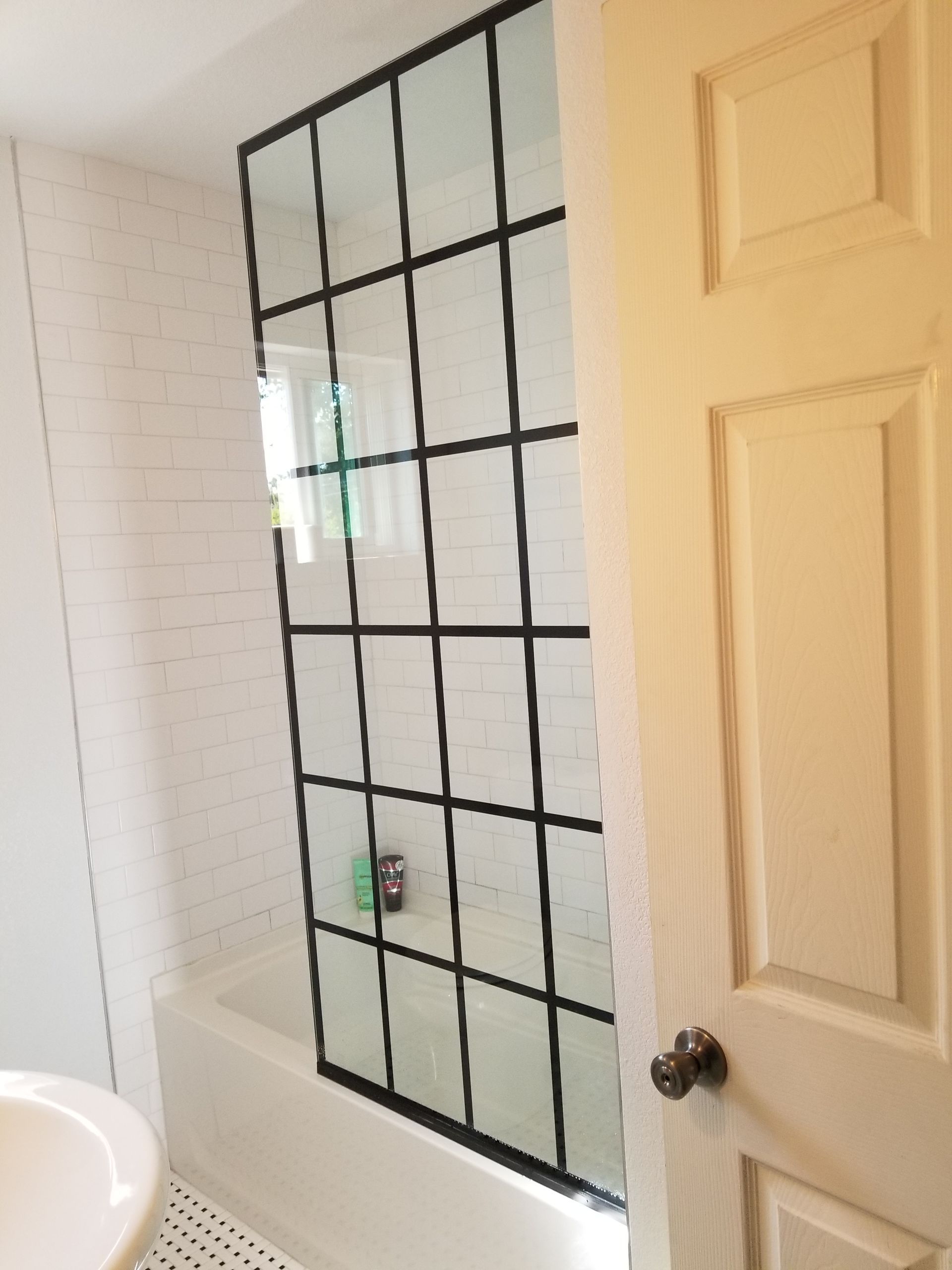 Bathroom with a black-framed shower screen, white brick wall, and a partially open door.