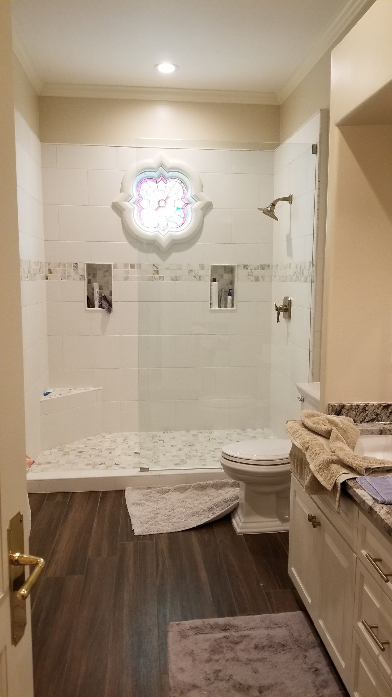 Bathroom with white tile shower, decorative window, and dark wood floor.