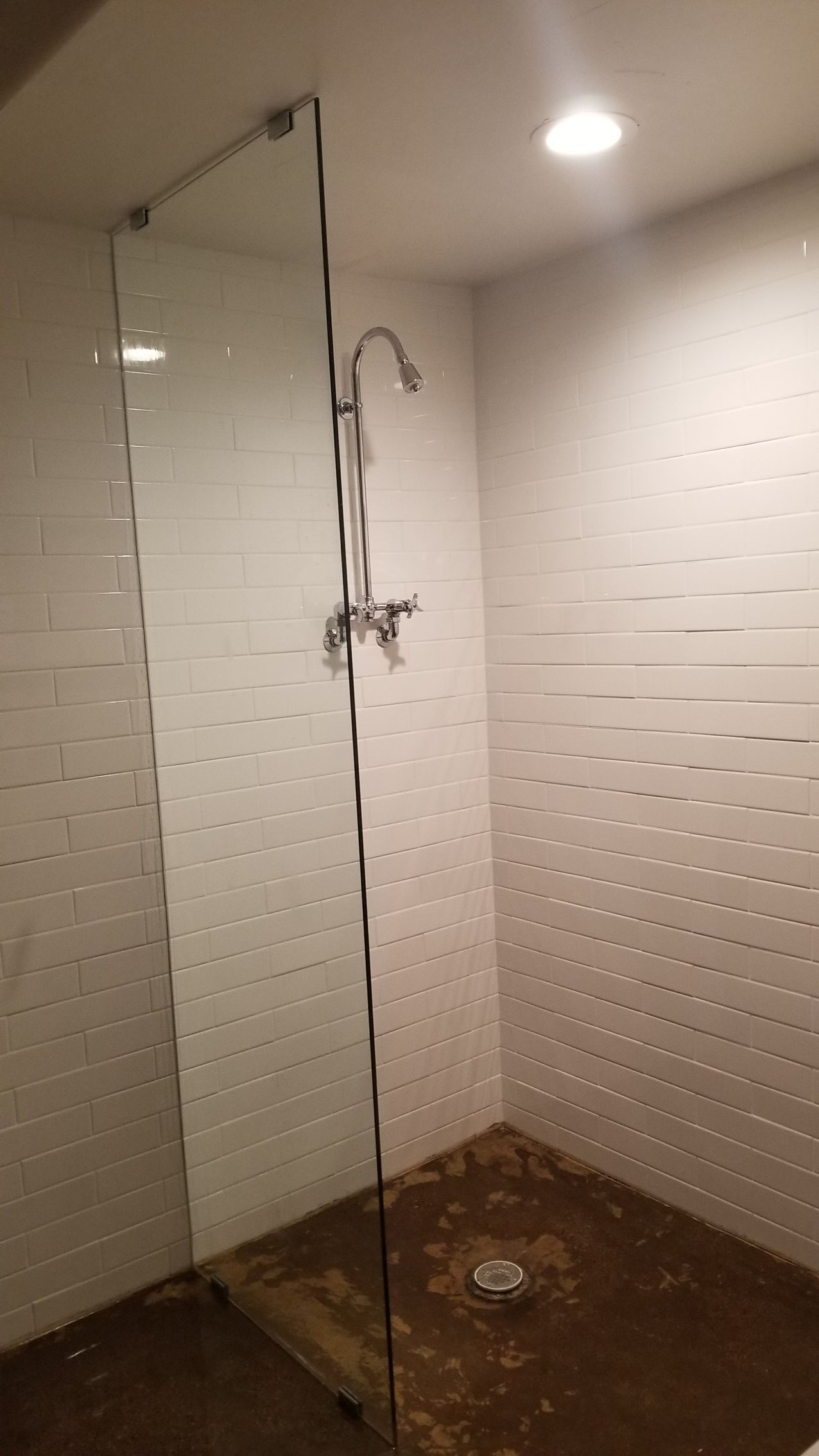 Shower stall with glass door, chrome fixtures, and white tiled walls. Dark floor.