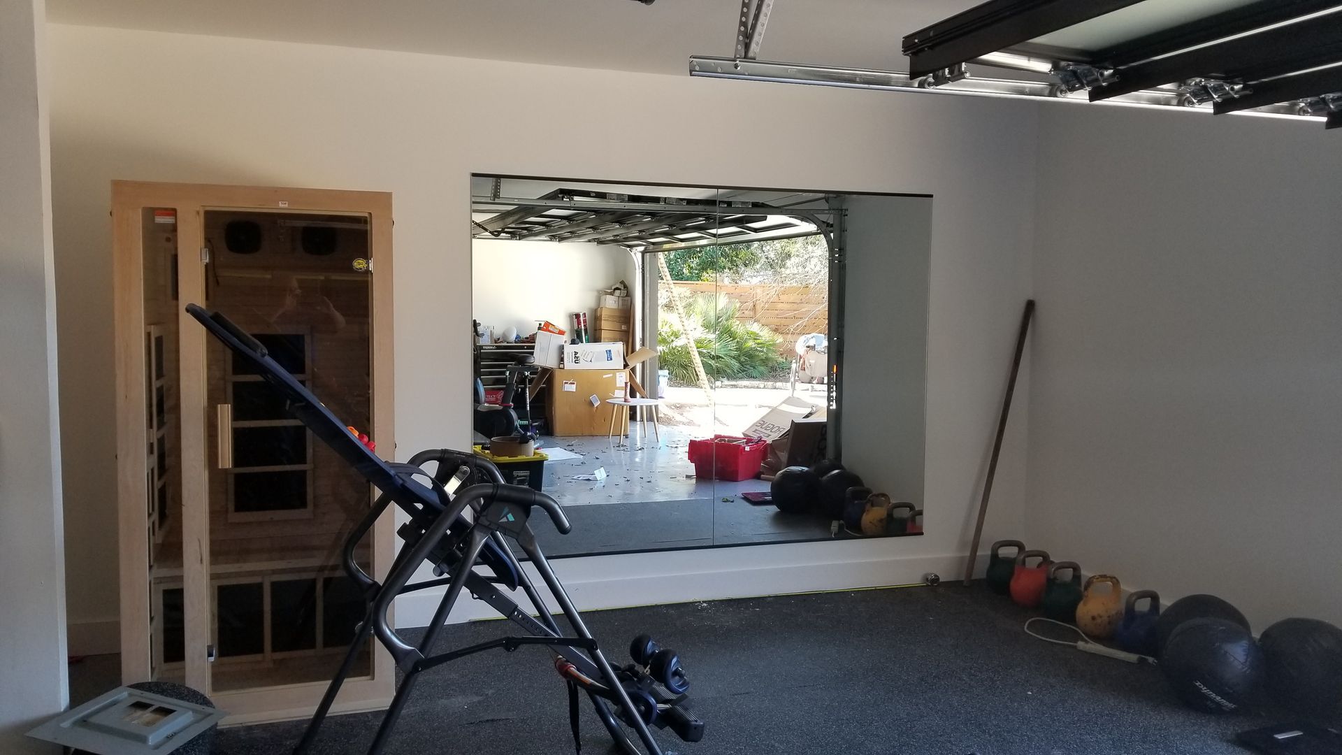 Home gym with a sauna, inversion table, weights, and a view through a large mirror.