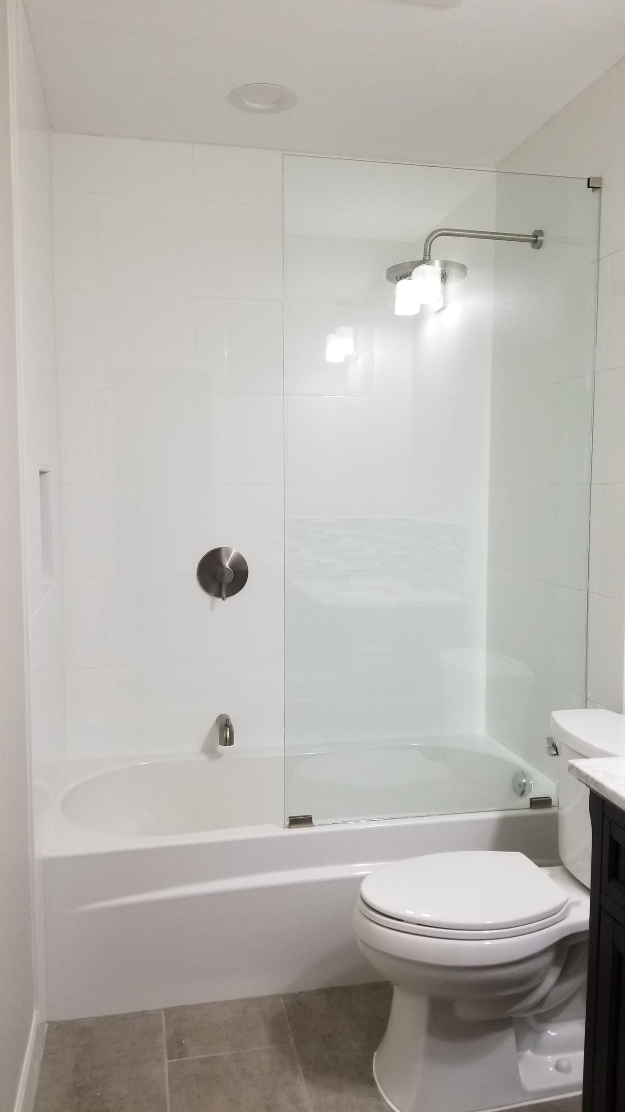 White bathroom with a bathtub, glass shower door, toilet, and silver fixtures.