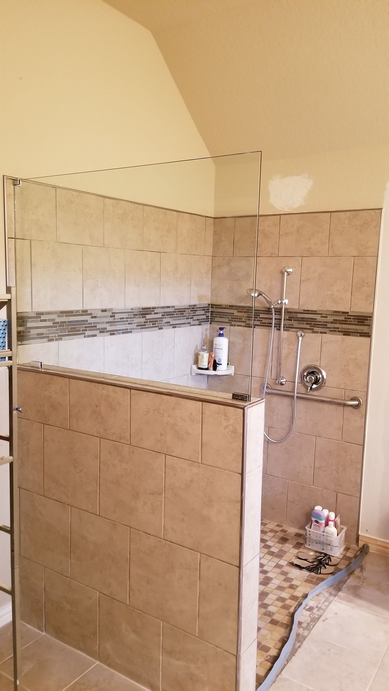Shower stall with beige tile, glass enclosure, and shower fixtures.
