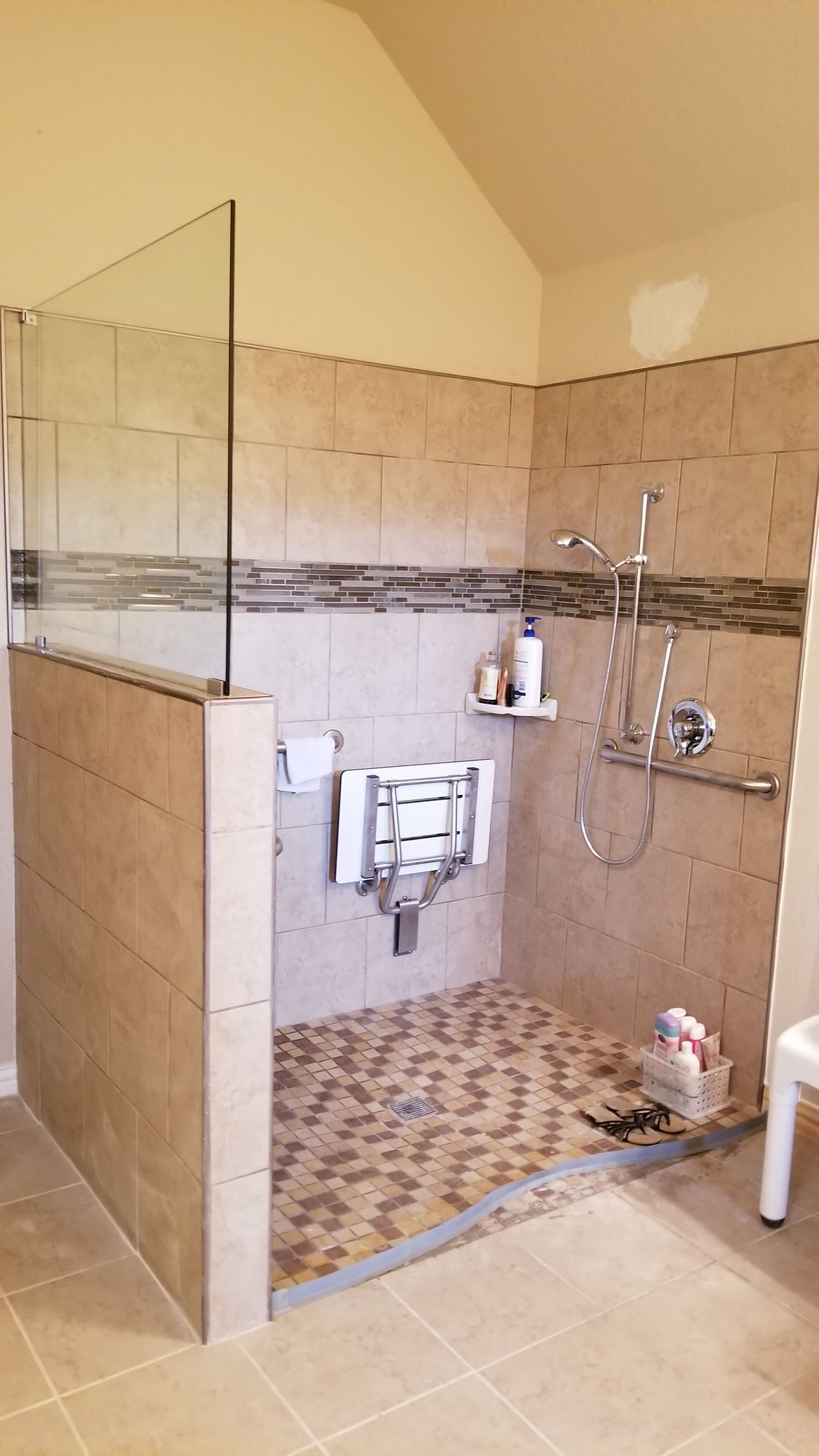 Accessible shower with glass panel, built-in seat, tiled walls, and pebble floor.