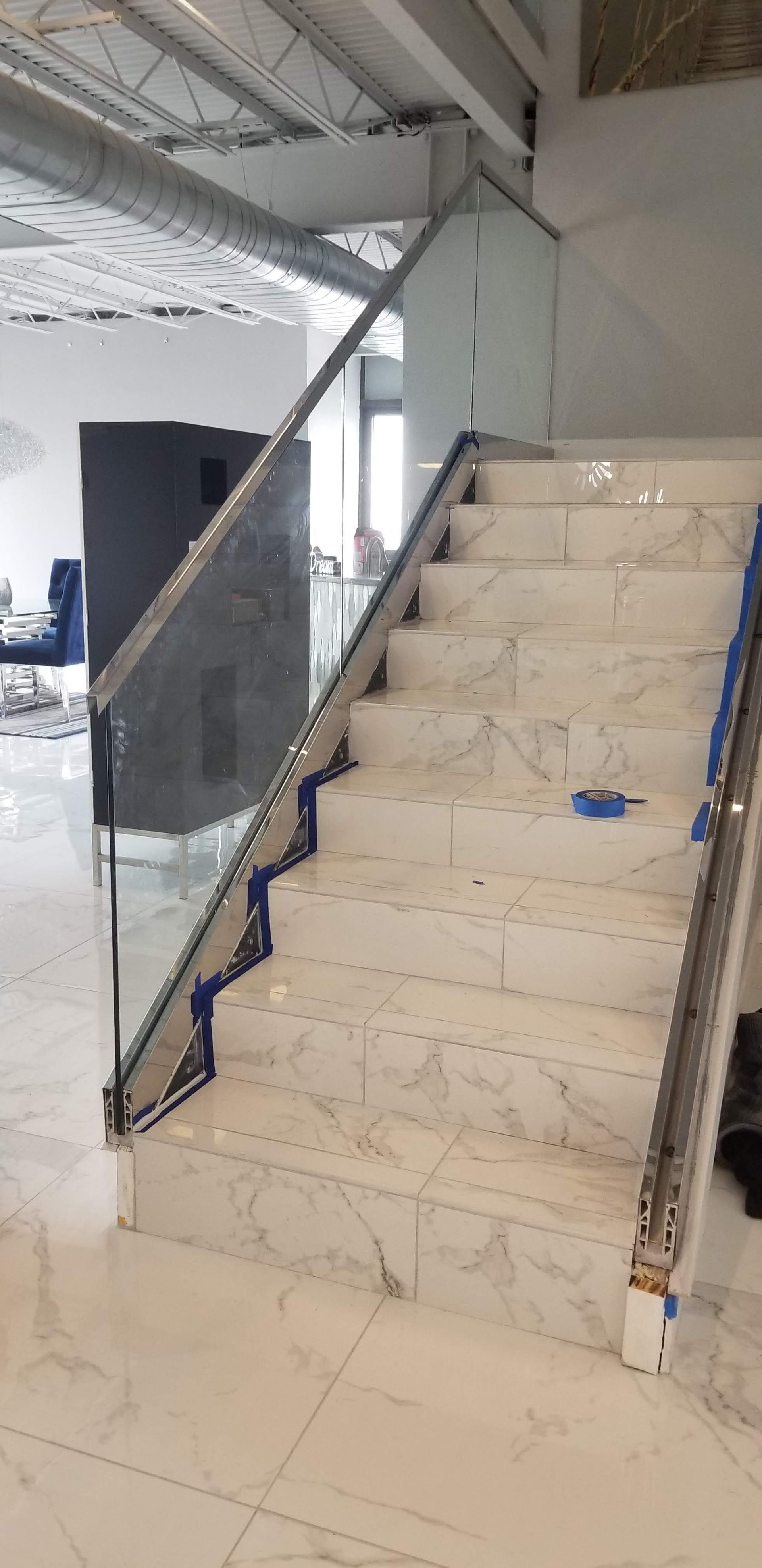 A marble staircase with glass railing. The stairs are lined with blue tape and the space has a modern feel.