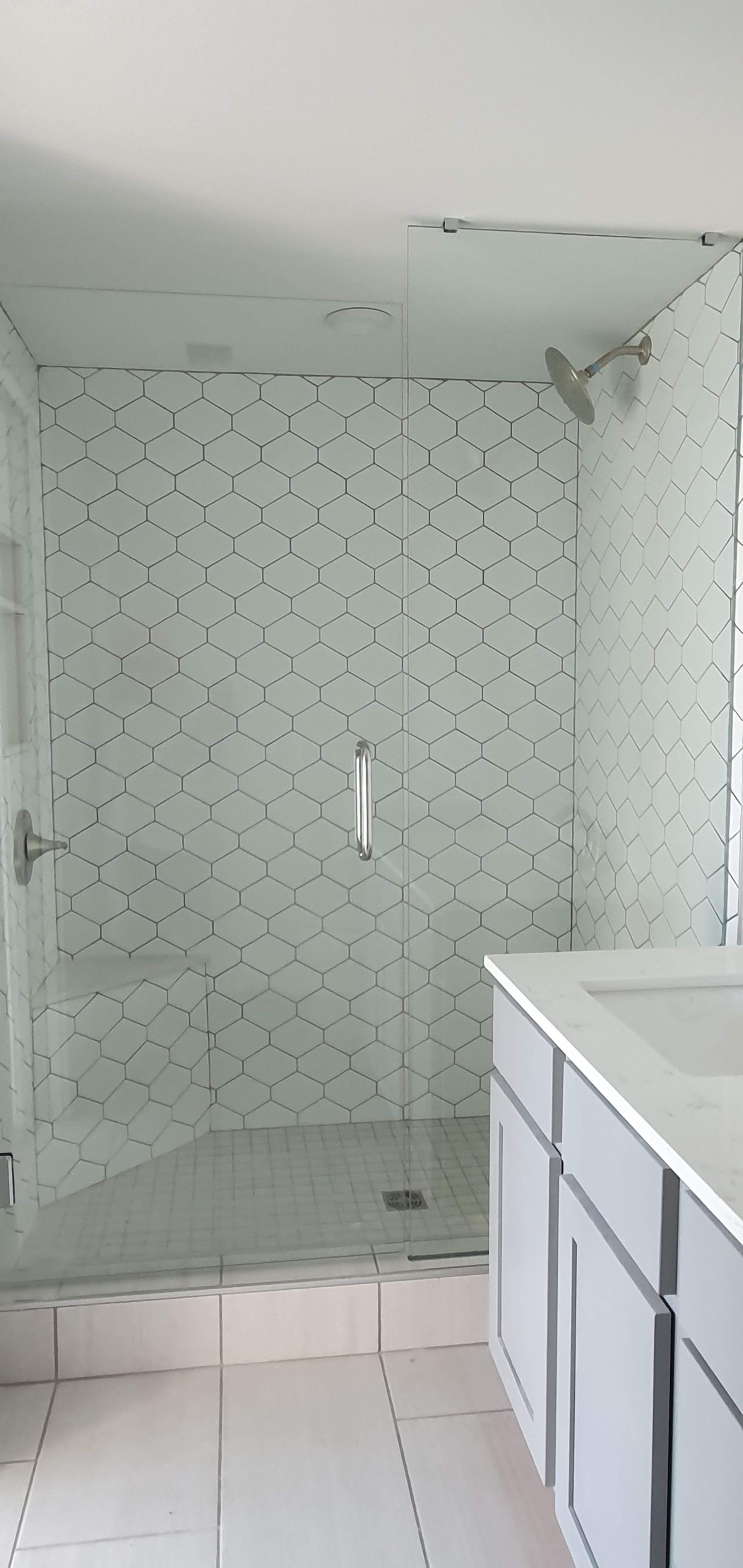 A bathroom with a glass shower and white hexagon tile, a gray vanity, and white floor tiles.