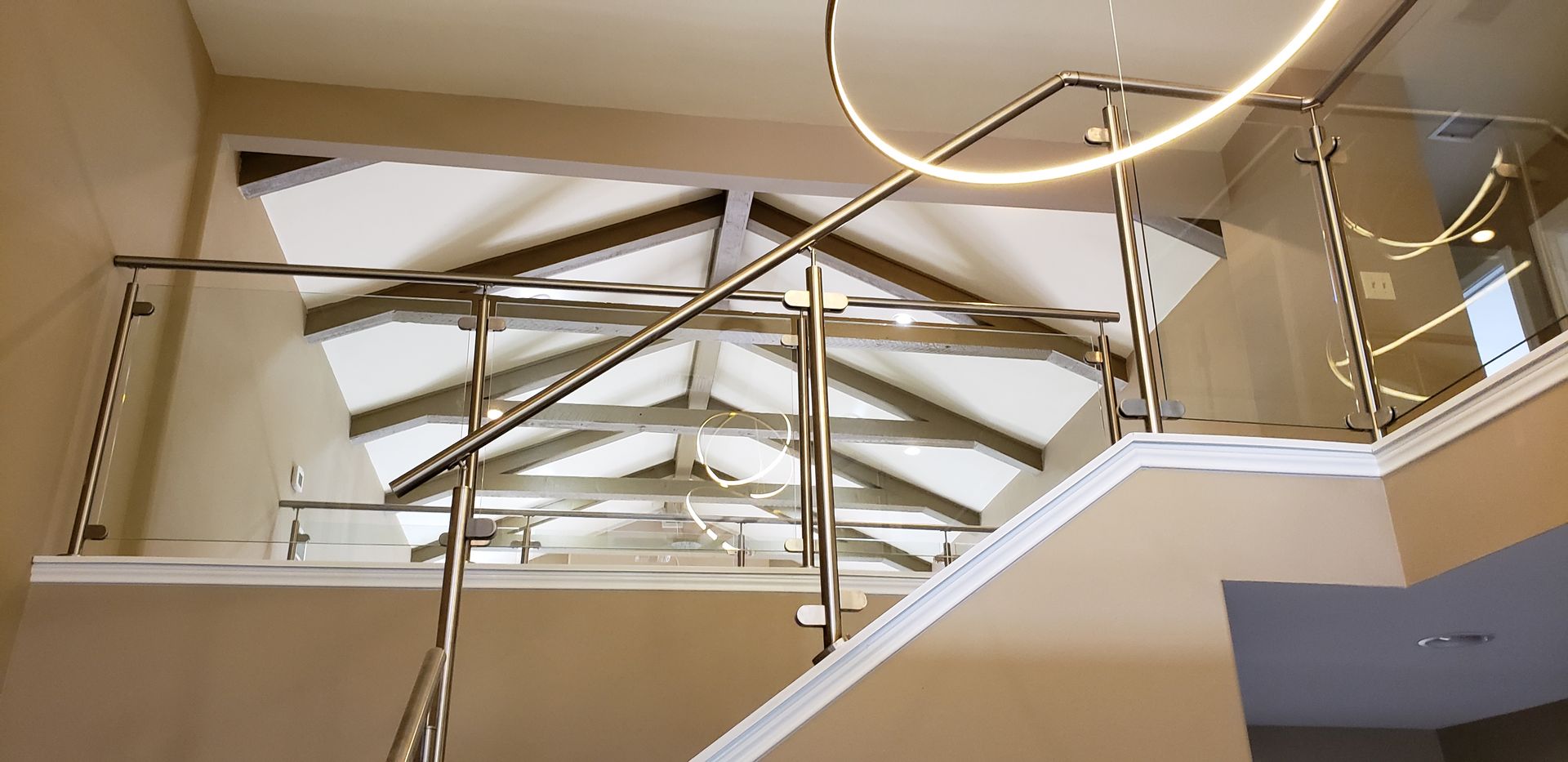 Staircase with stainless steel handrails, glass panels, and a decorative ceiling. Beige walls, white trim.