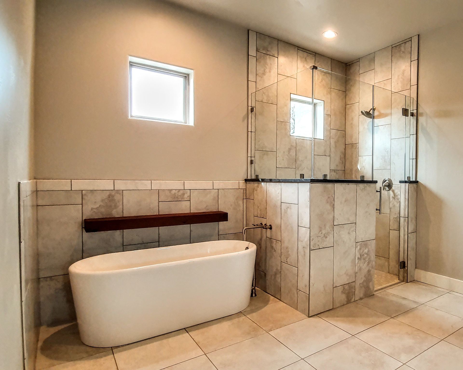 Bathroom with a white freestanding tub, glass shower, and tiled walls and floor.