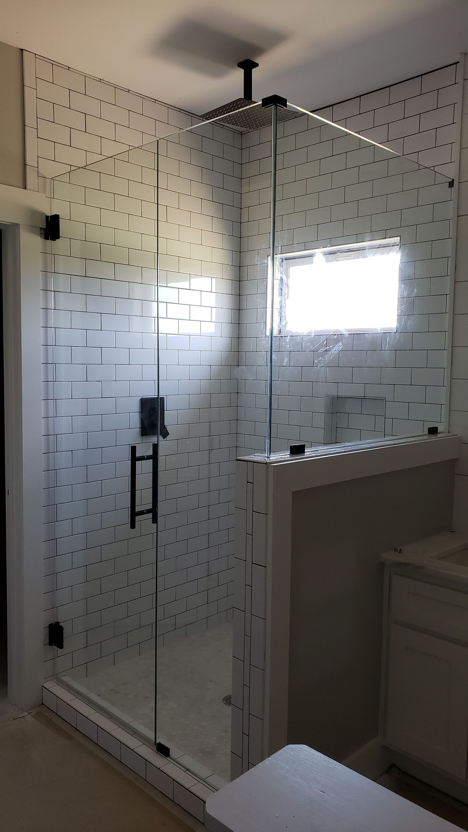 Glass shower enclosure with black fixtures and white tiled walls.