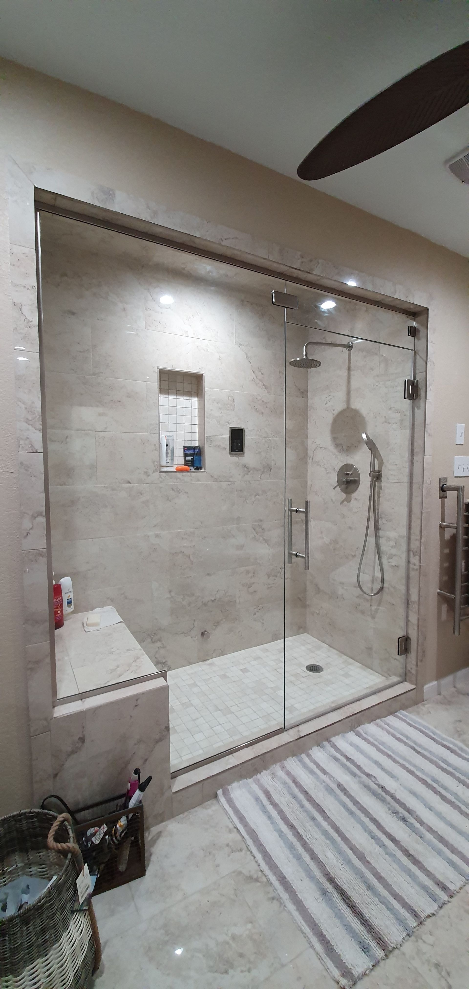 A spacious, modern bathroom with a glass-enclosed shower featuring beige tiles, a bench, and a striped rug.