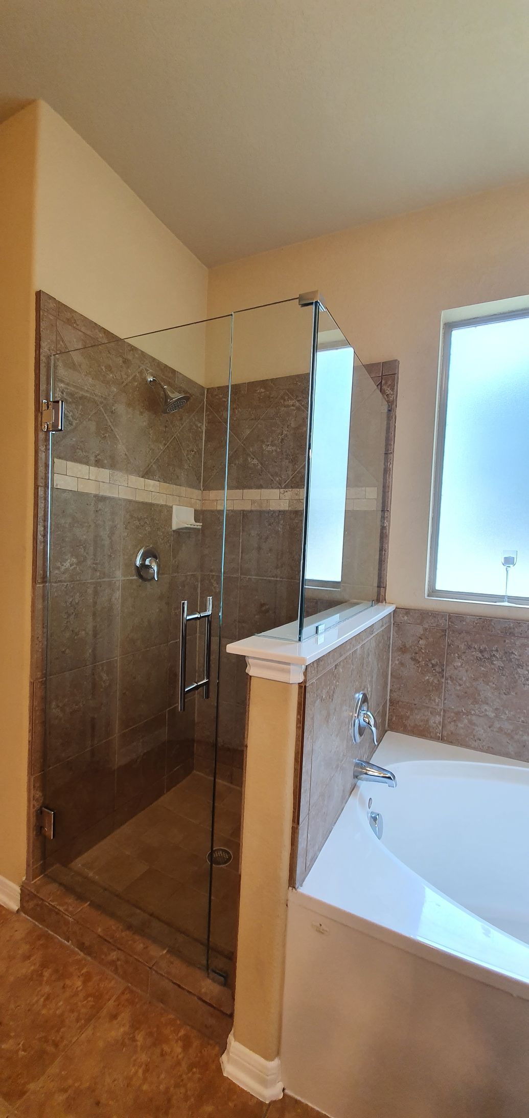 Bathroom with a shower and a bathtub. The shower has glass doors and tile walls. The bathtub is white.