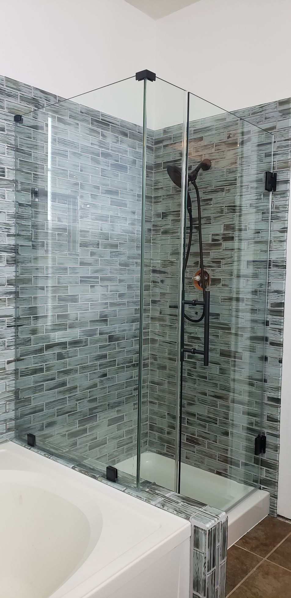 Glass shower enclosure with mosaic tile walls and a white bathtub.