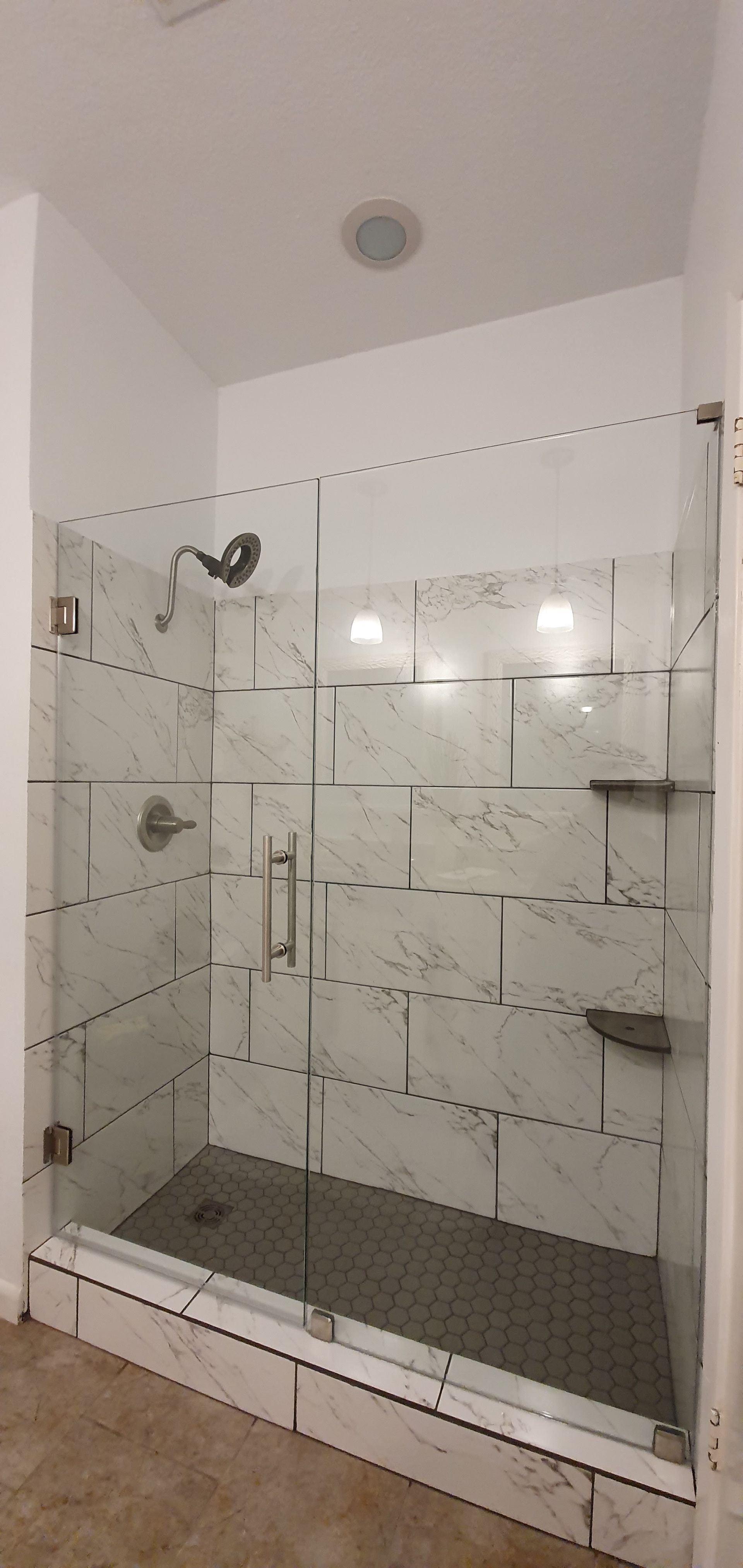A modern shower with clear glass doors, white brick-like tiles, and silver fixtures.