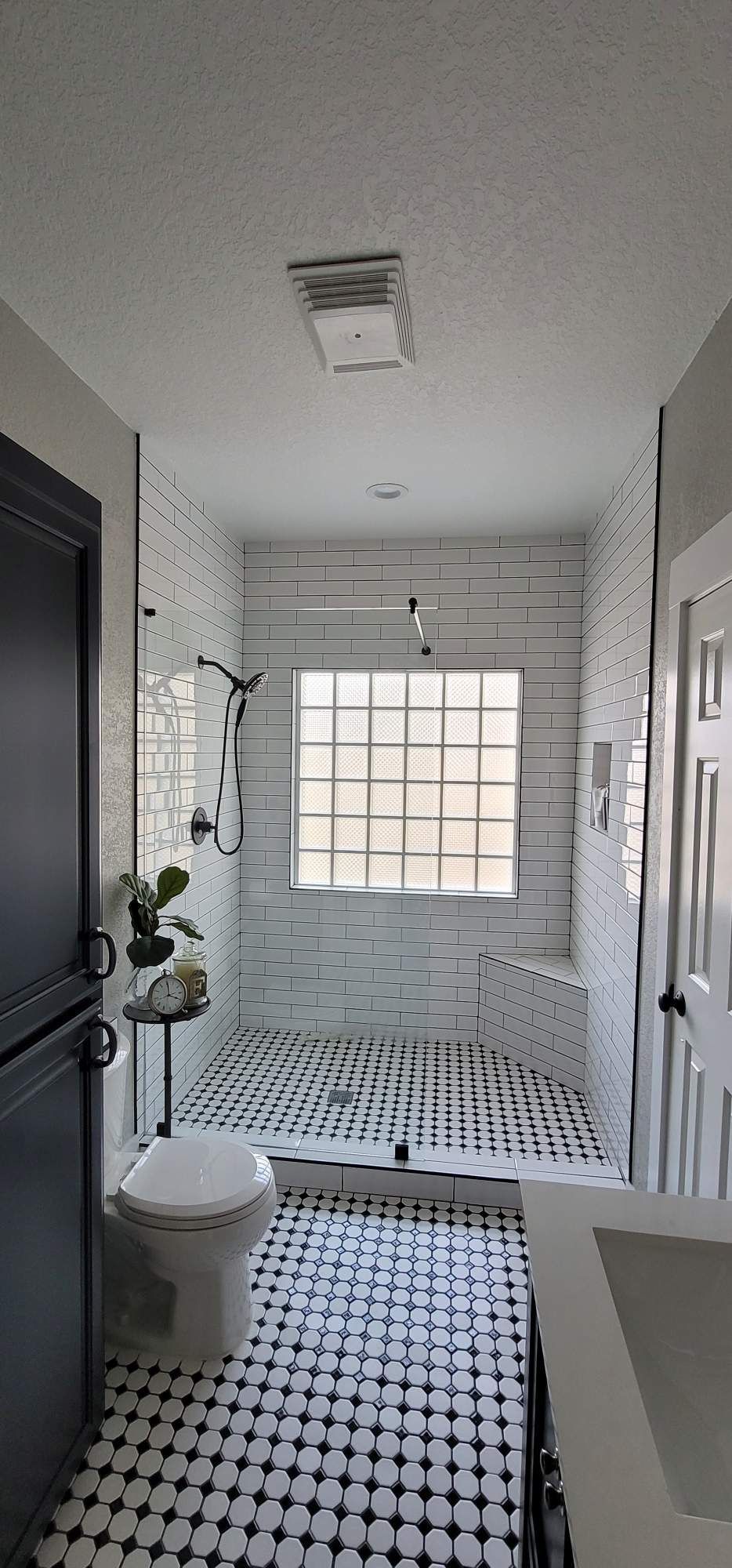 Bathroom with black and white tile flooring, shower, toilet, and a window.