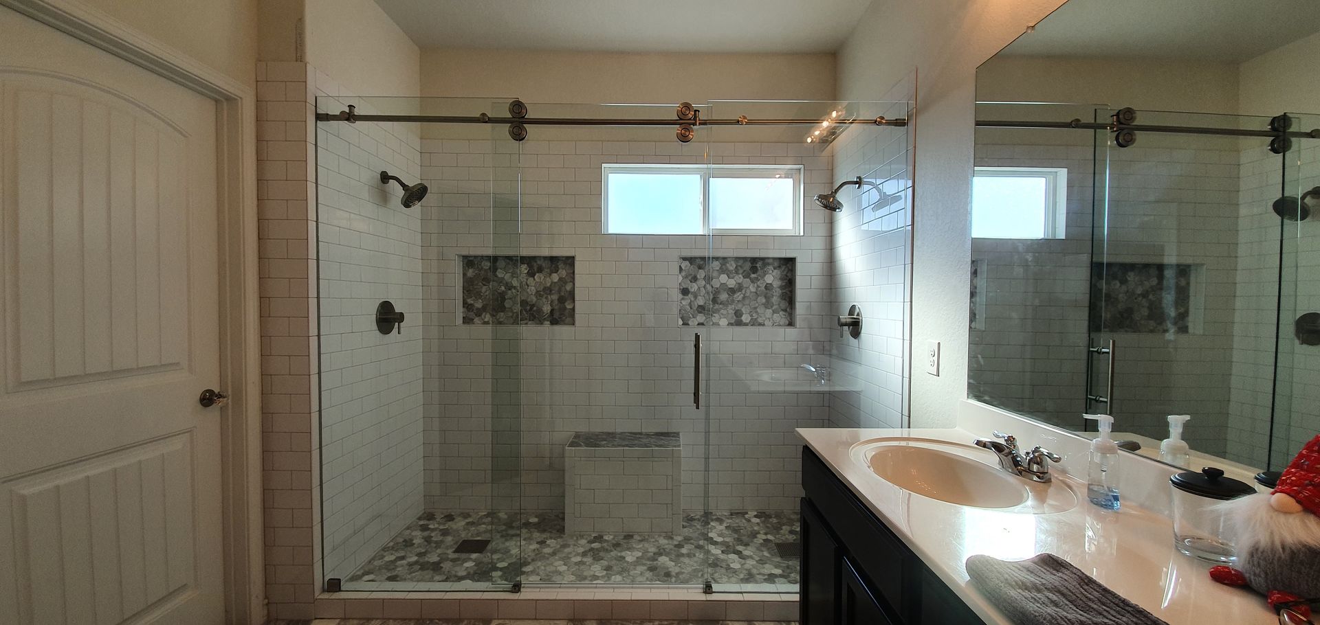 Bathroom with a walk-in shower, vanity, large mirror, and a window. Neutral tones and clean design.