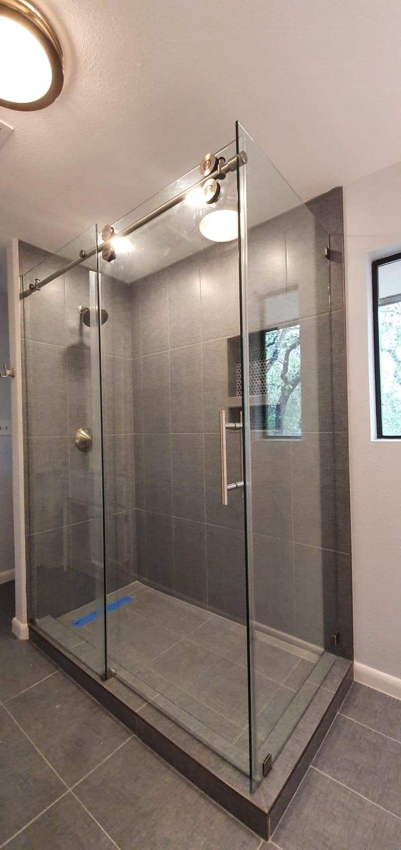 A modern shower with sliding glass doors and gray tile walls and floor.