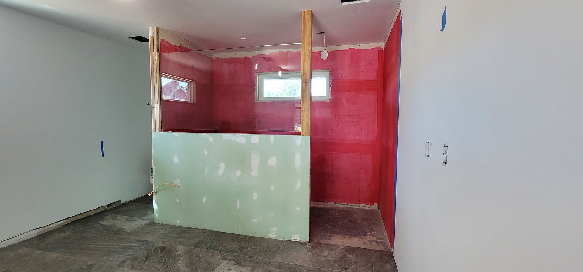 Interior of a room under construction with green and red walls. Wooden beams frame a shower area.
