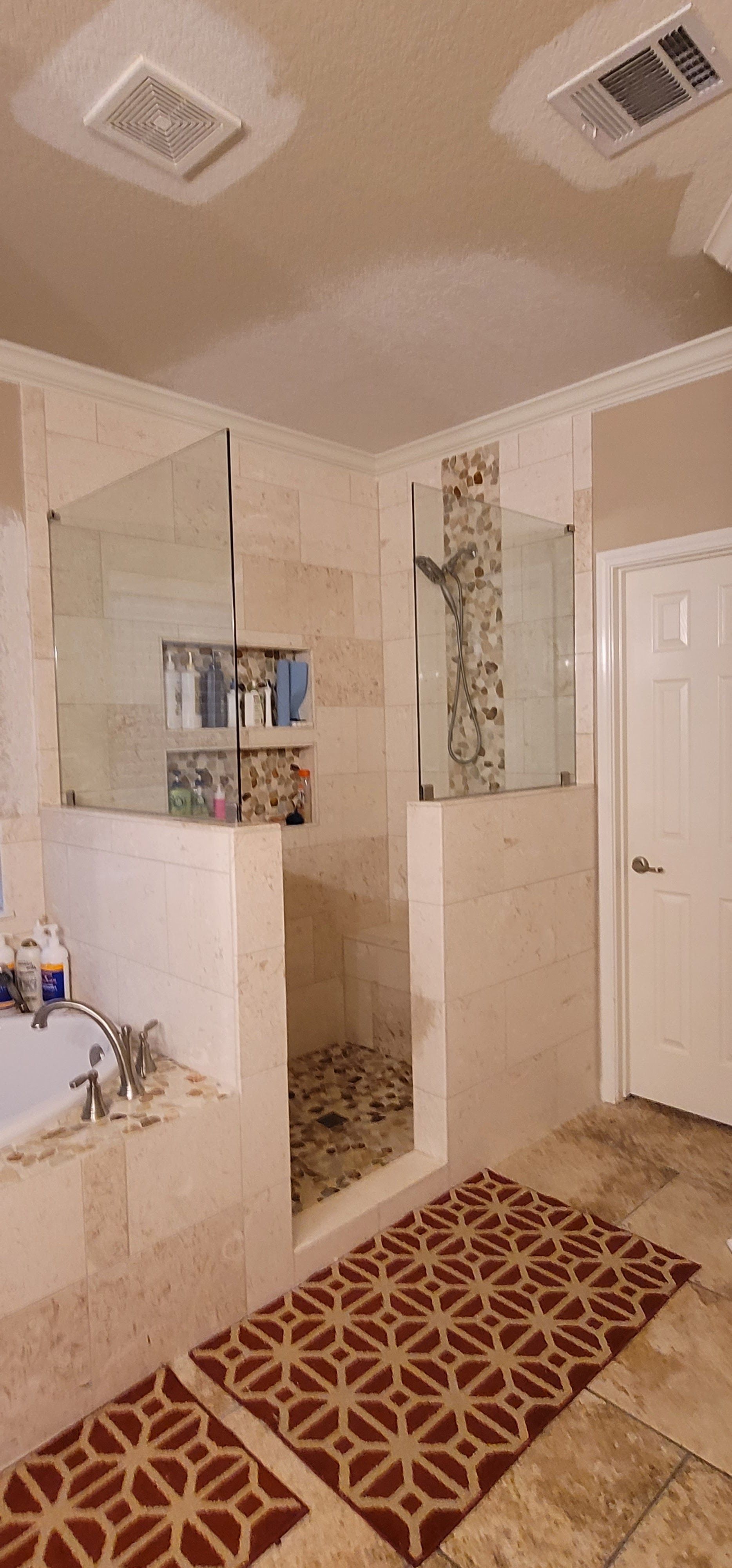 Bathroom with a walk-in shower. The shower has glass doors and a stone floor. A patterned rug is on the floor.