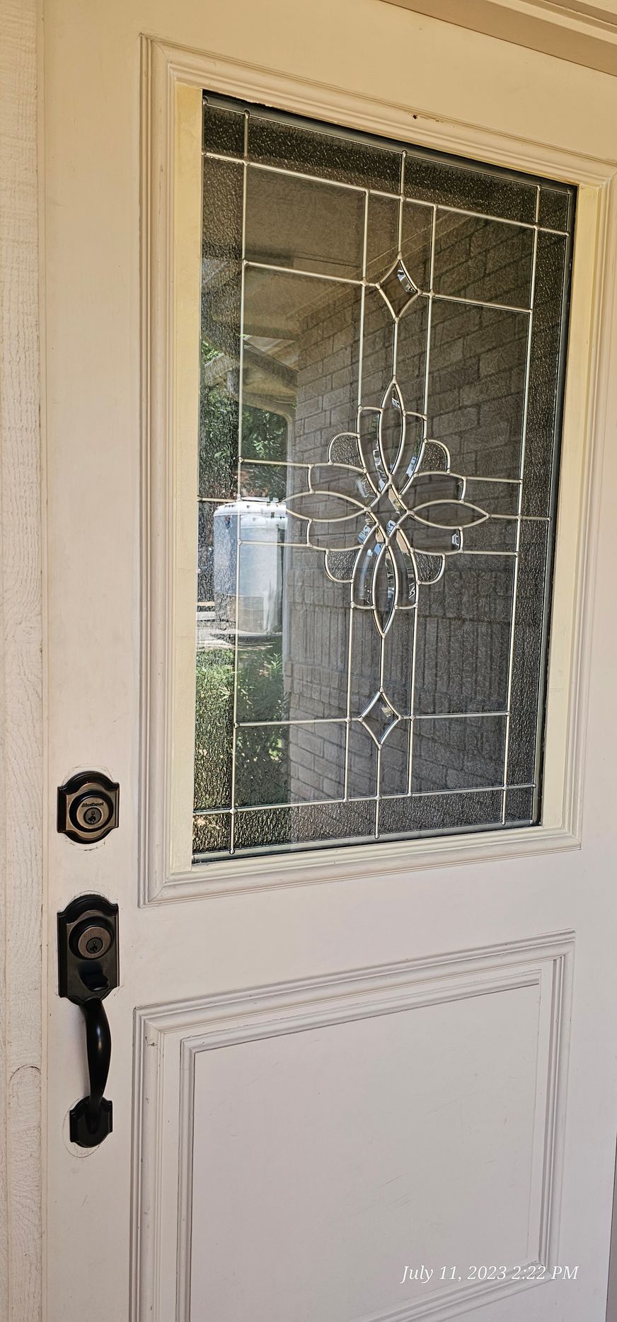 White front door with decorative glass panel and black door hardware.