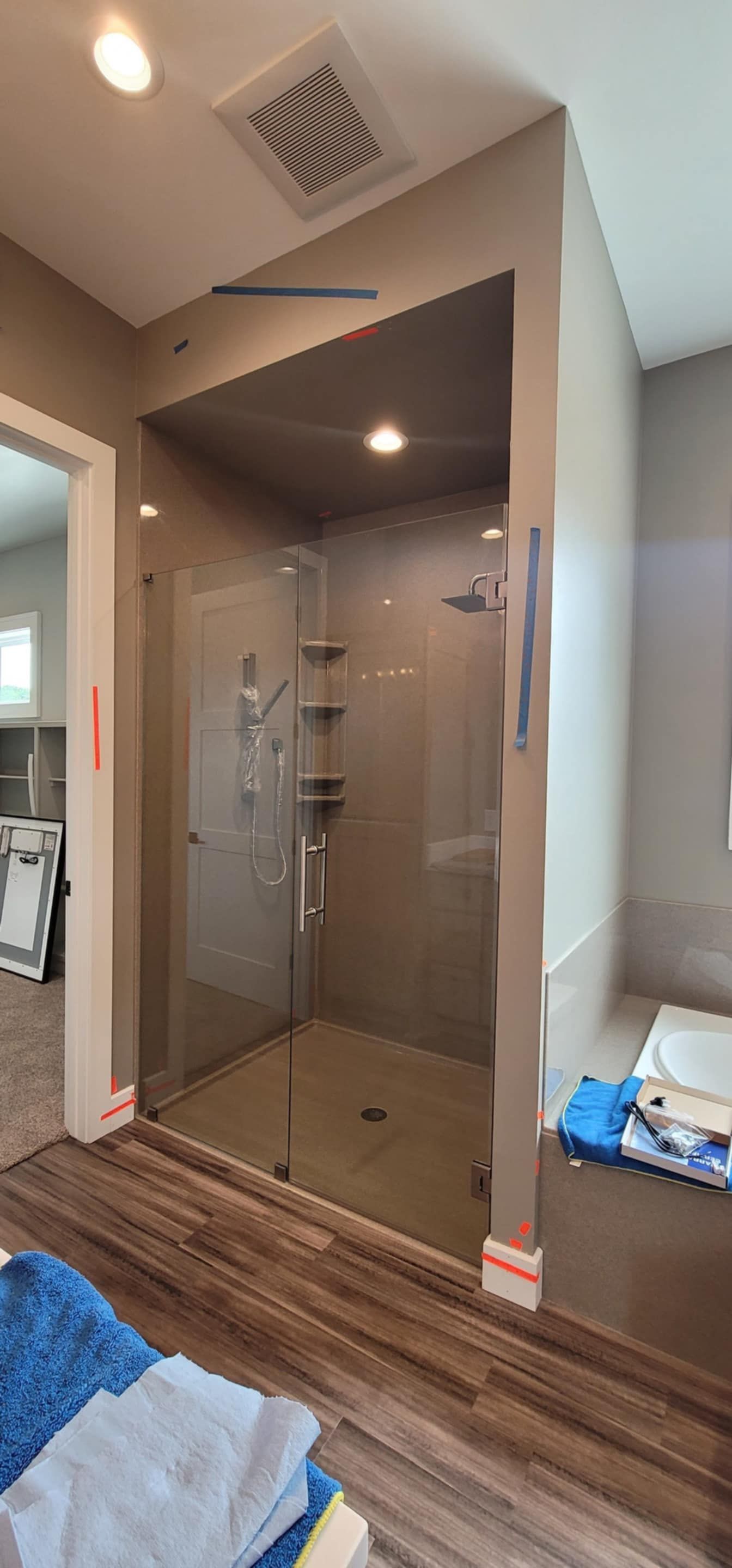 Bathroom with a walk-in glass shower, brown wood-look flooring, and a towel on the floor.