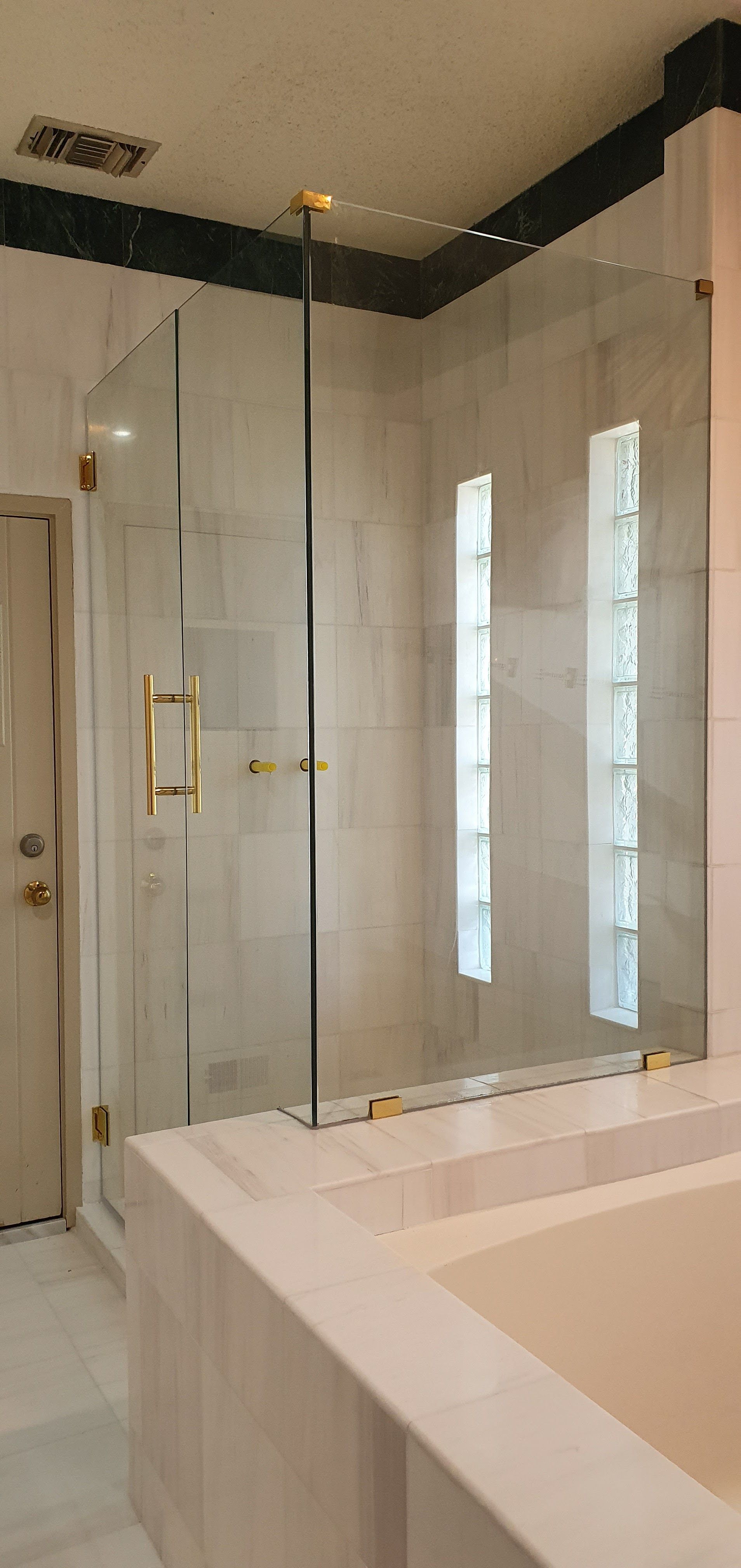 A modern bathroom with a glass-enclosed shower, a white bathtub, and light-colored tile walls.