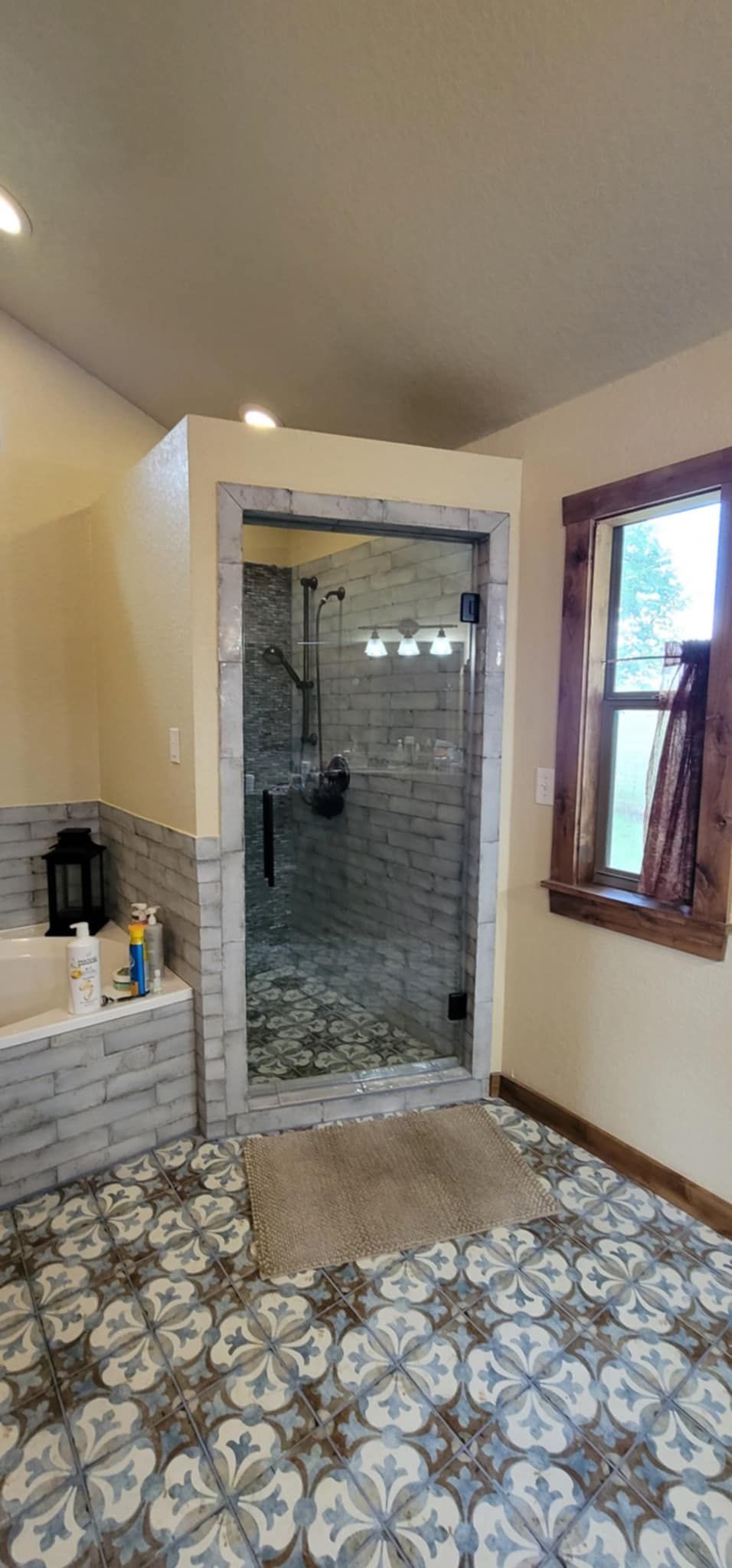 Bathroom with patterned tile floor, glass shower, and window with wood frame.