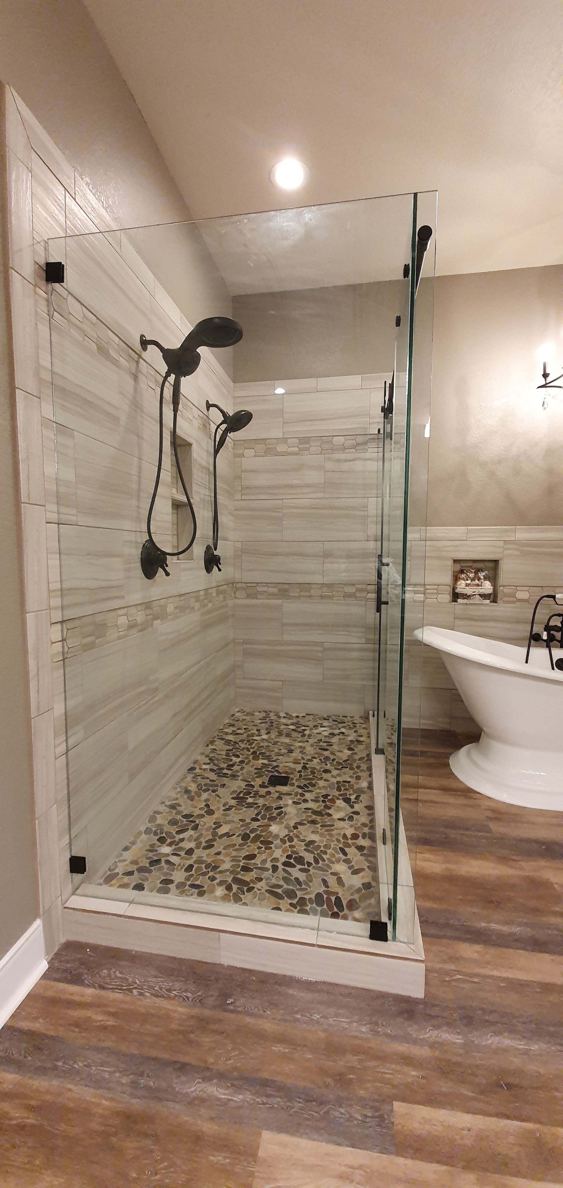 A modern bathroom with a glass-enclosed shower, pebbled floor, and wood-look flooring.