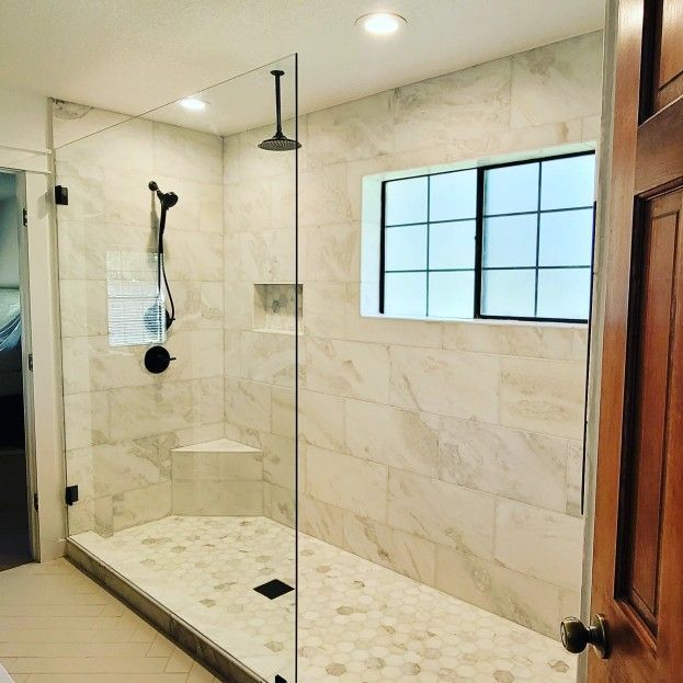 Modern bathroom with glass shower enclosure, marble tile, and window.