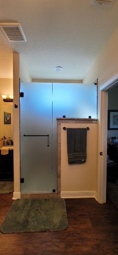 Bathroom with a frosted glass shower enclosure and a green bath mat on dark wood flooring.