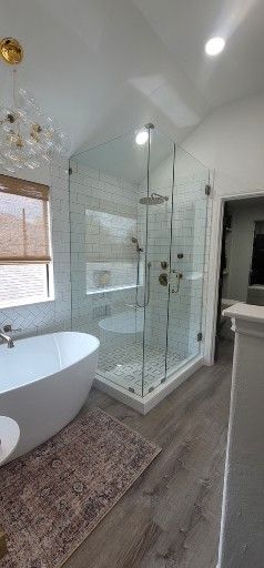 Modern bathroom with a glass shower, white soaking tub, and decorative rug.