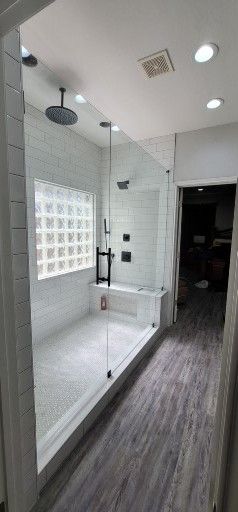 Modern bathroom with glass shower, white subway tile, a bench, and gray wood flooring.