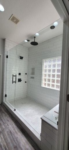 Modern bathroom with a glass shower, white tile walls, and a window.
