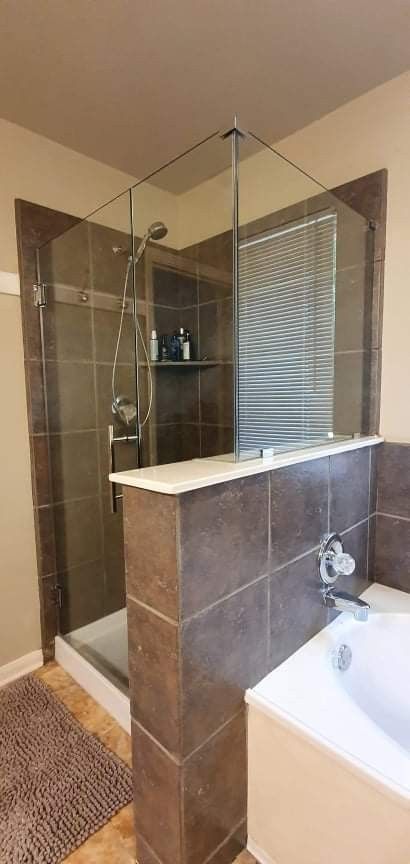 A bathroom with a tiled shower stall and a bathtub. Brown tiles line the shower.
