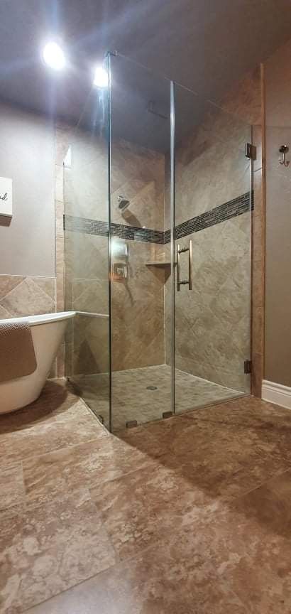 Bathroom with a glass shower, soaking tub, and stone tile.
