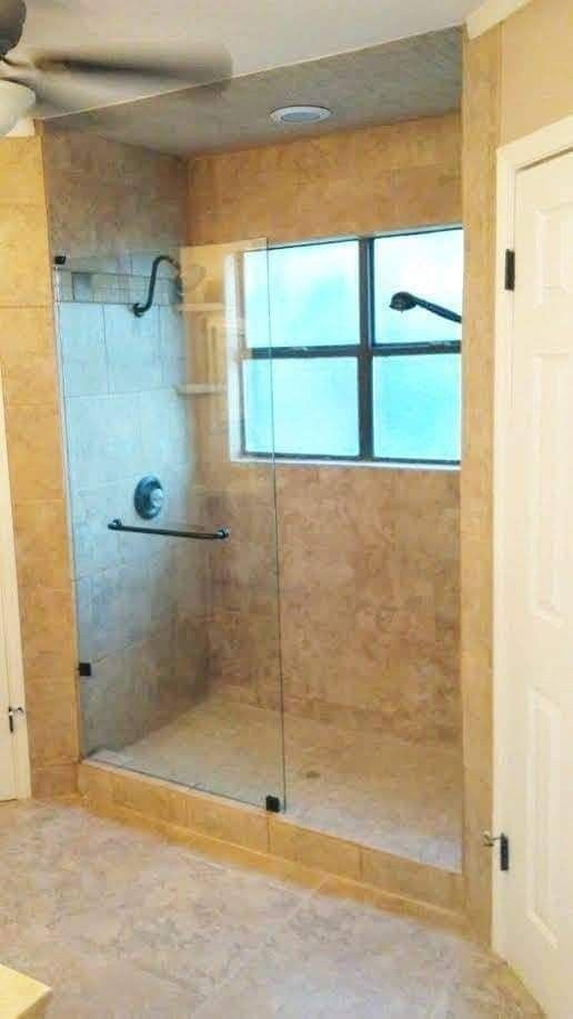 Walk-in shower with glass door and tile walls, a window, and chrome fixtures.
