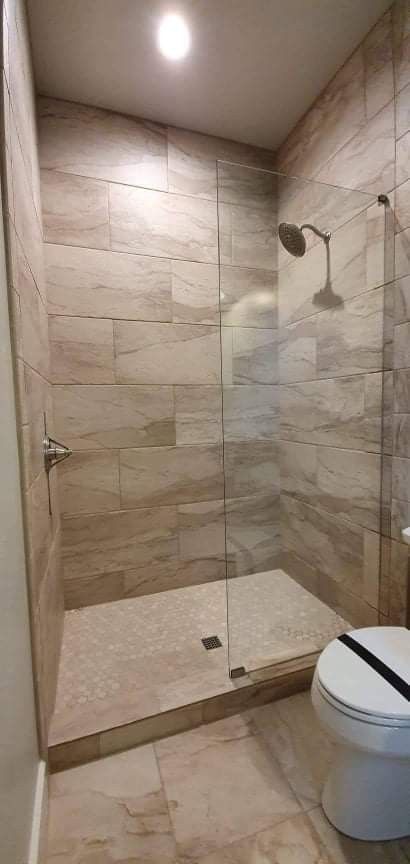 A tiled shower with a glass door, showerhead, and a toilet.