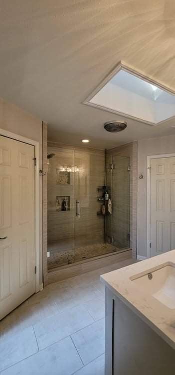 Bathroom with glass shower, white cabinets, and a skylight.