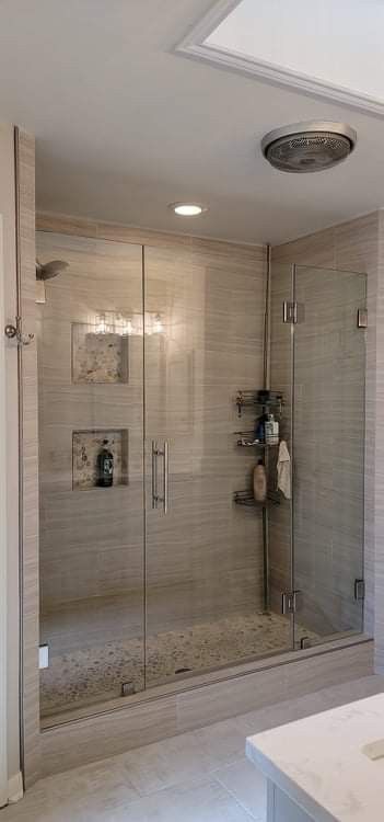 Modern shower with glass doors, stone tile walls and floor, built-in shelves, and a rain showerhead.