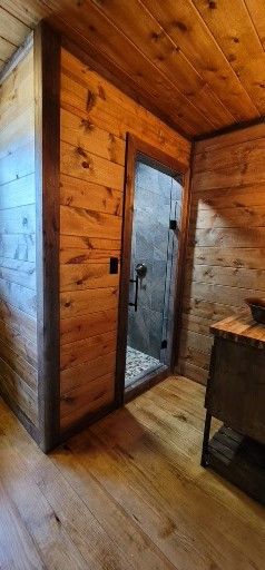 Wooden bathroom with glass shower door, wooden walls, floors, and ceiling.