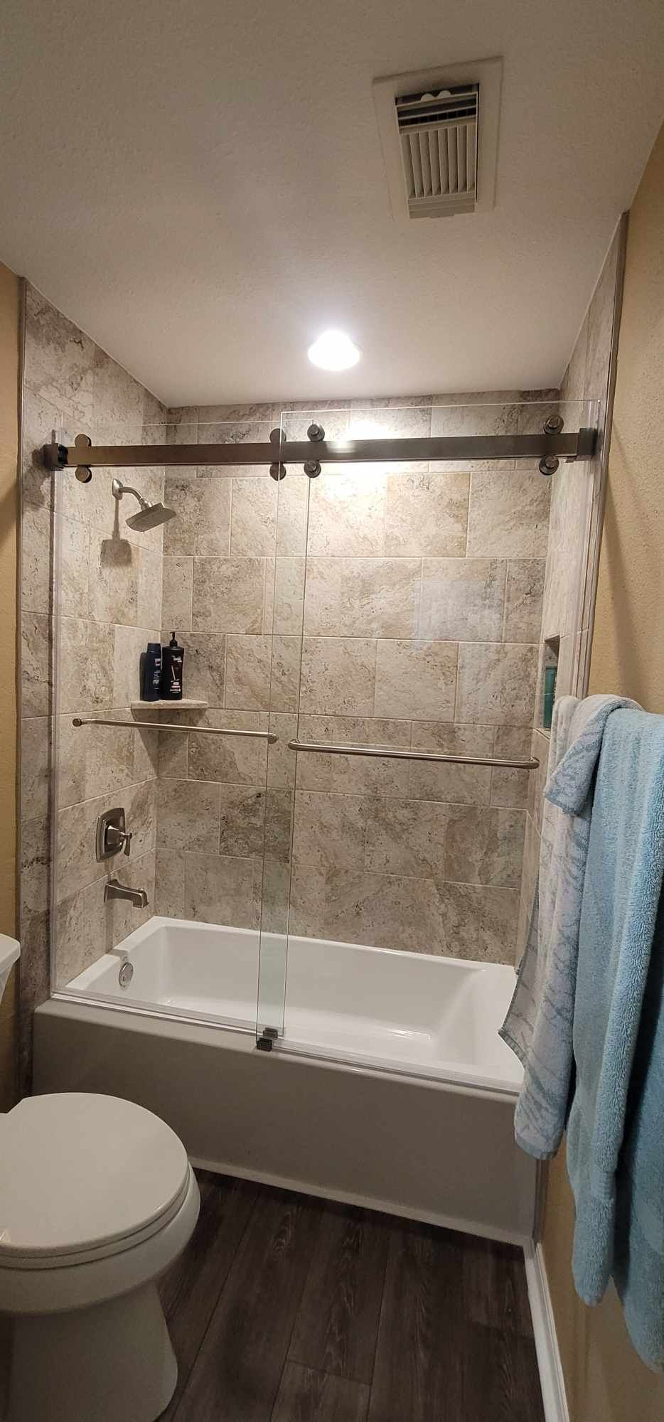 Bathroom with a tub, shower, and sliding glass door. Gray stone-like wall tile and dark wood-look floor.