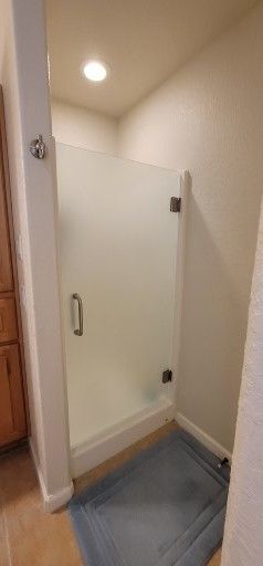 A glass shower door with a handle and hinges, inside a bathroom with a blue bath mat.