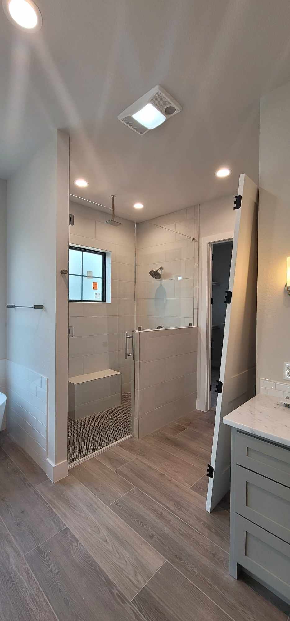 Modern bathroom with a glass shower, gray tiled walls, and wood-look flooring.