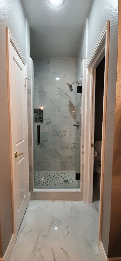 Narrow bathroom hallway with shower and two white doors.