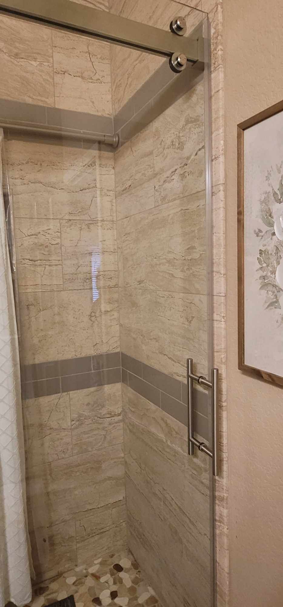 A shower stall with sliding glass doors, tile walls, and a pebble floor.