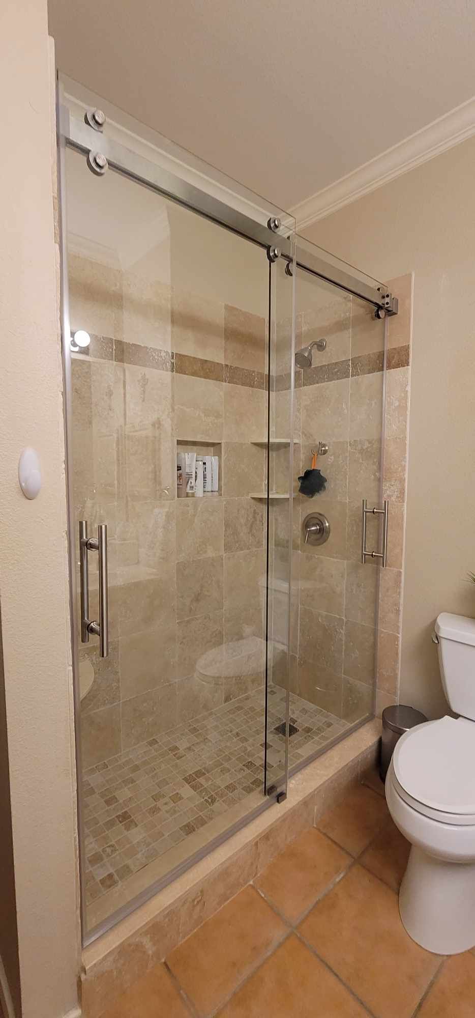 A modern glass shower with a sliding door, tiled walls, and a toilet in a bathroom.