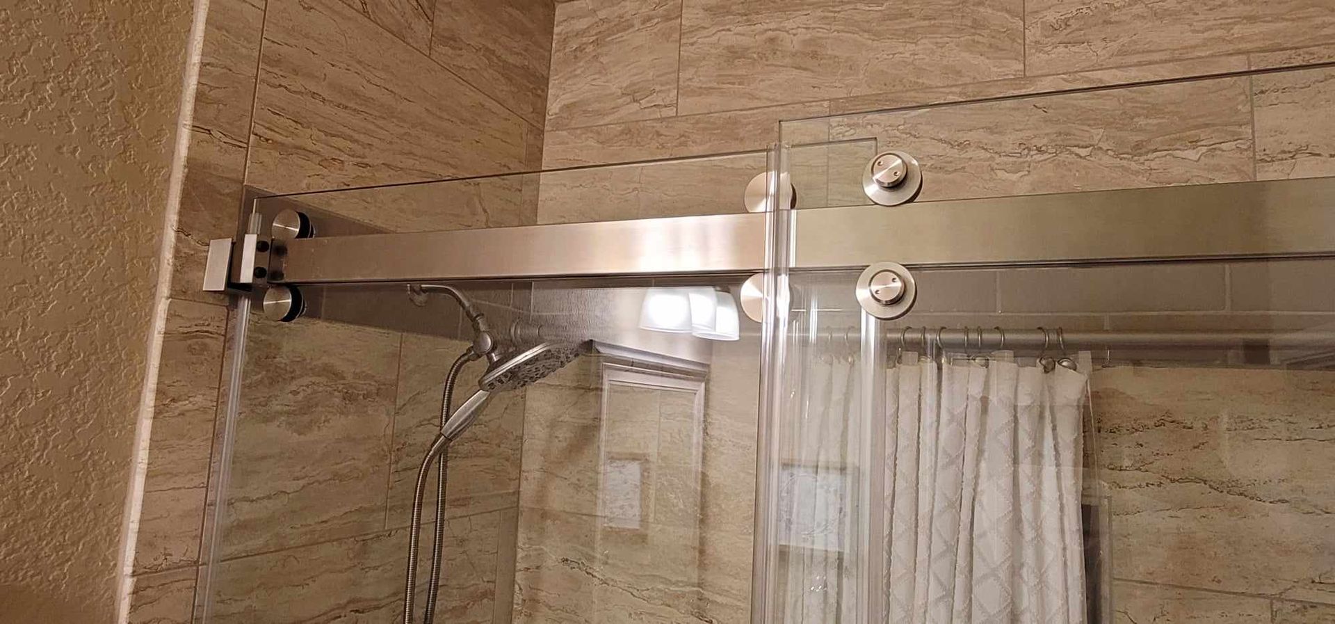 Shower with a glass door, silver hardware, and stone tile walls. Water is running.