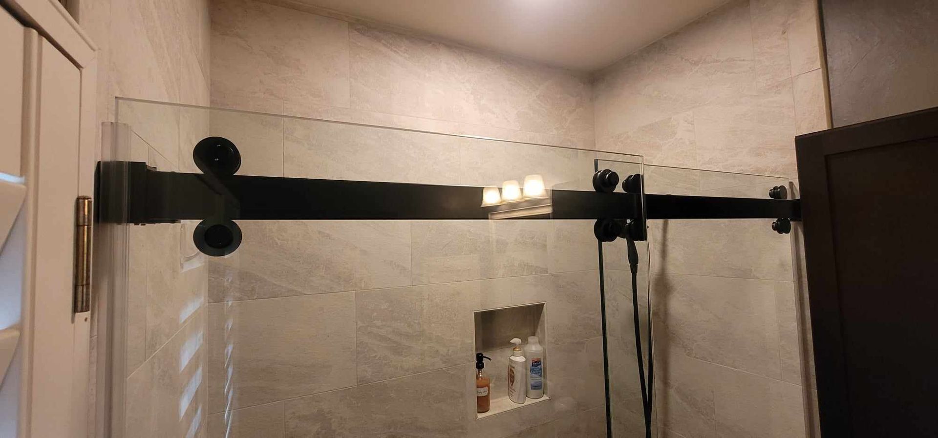 A frameless glass shower door with black hardware, on a tile-walled shower.