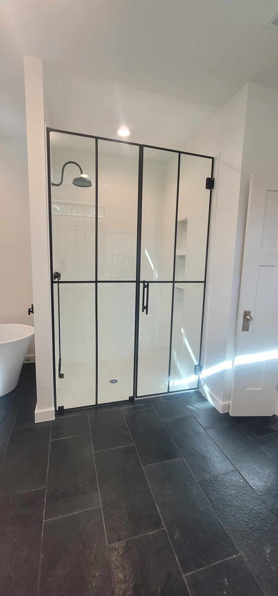 Modern bathroom with black-framed glass shower doors, dark floor tiles, and white walls.