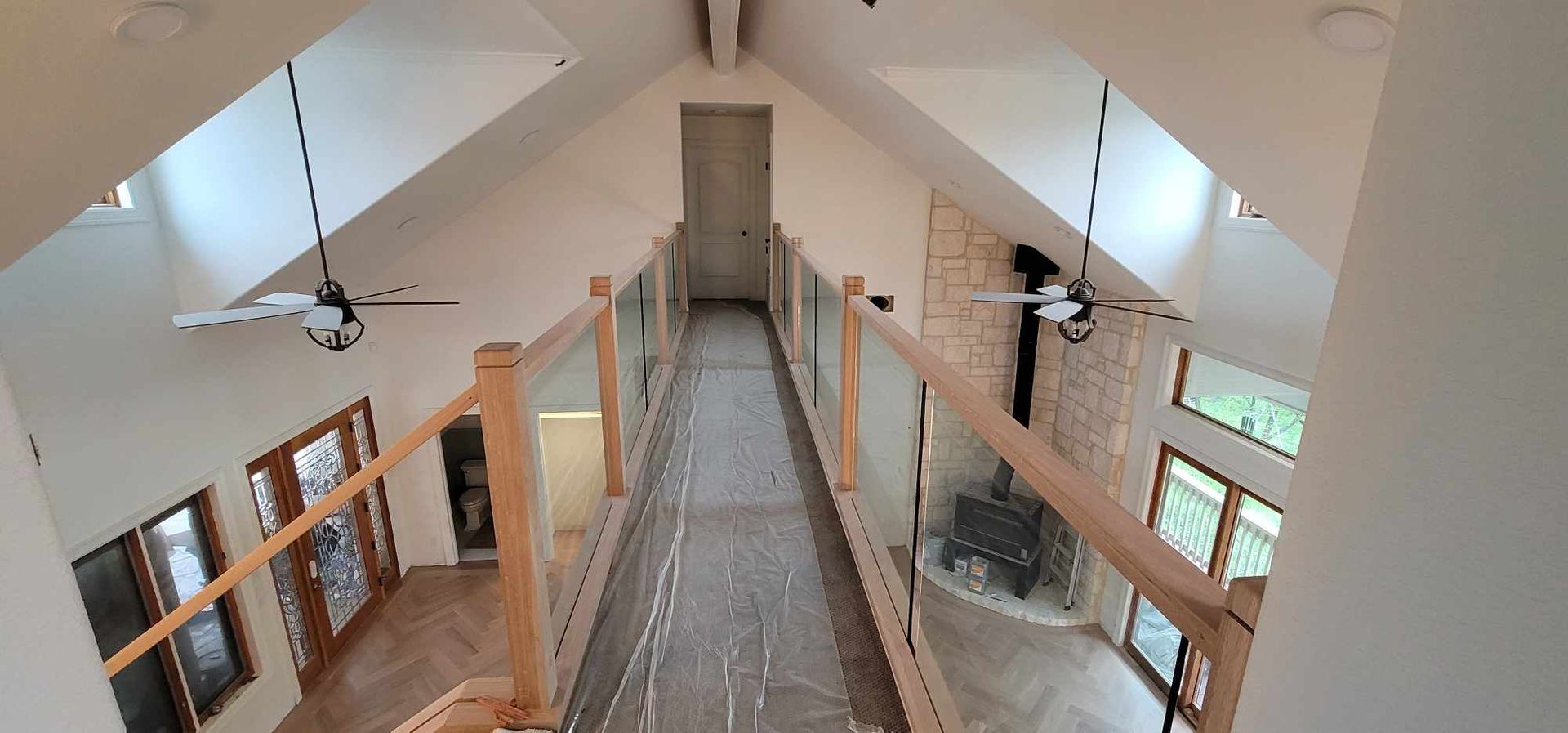 Interior view of a house with a high ceiling, a bridge with glass railings, and a fireplace.